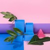 Vivid arrangement of green leaves in blue geometric containers on a pastel backdrop.